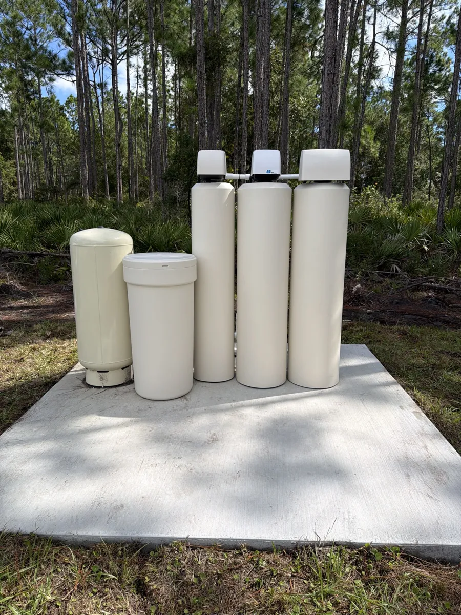 Multi-tank well water treatment system on a concrete pad near pine trees